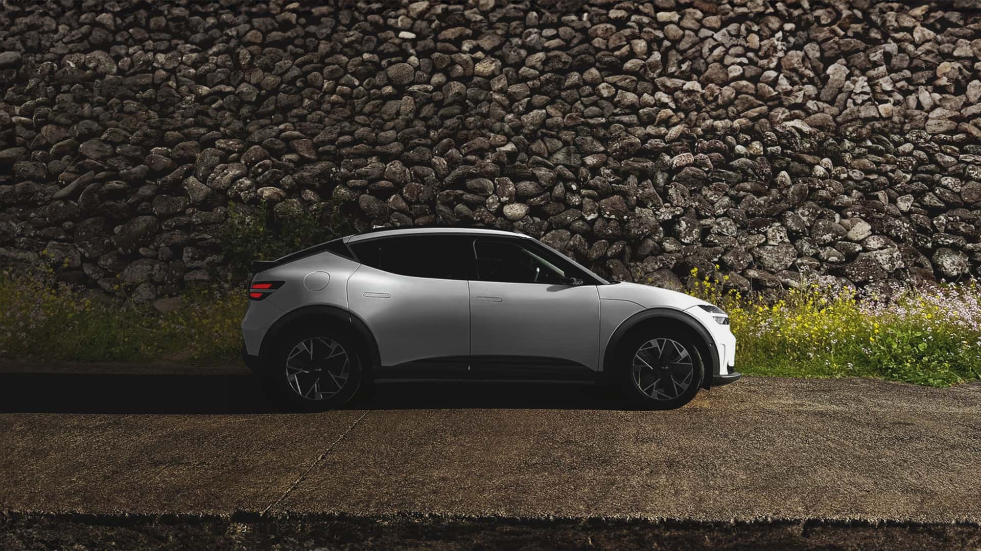 A white compact electric crossover parked beside a stone wall