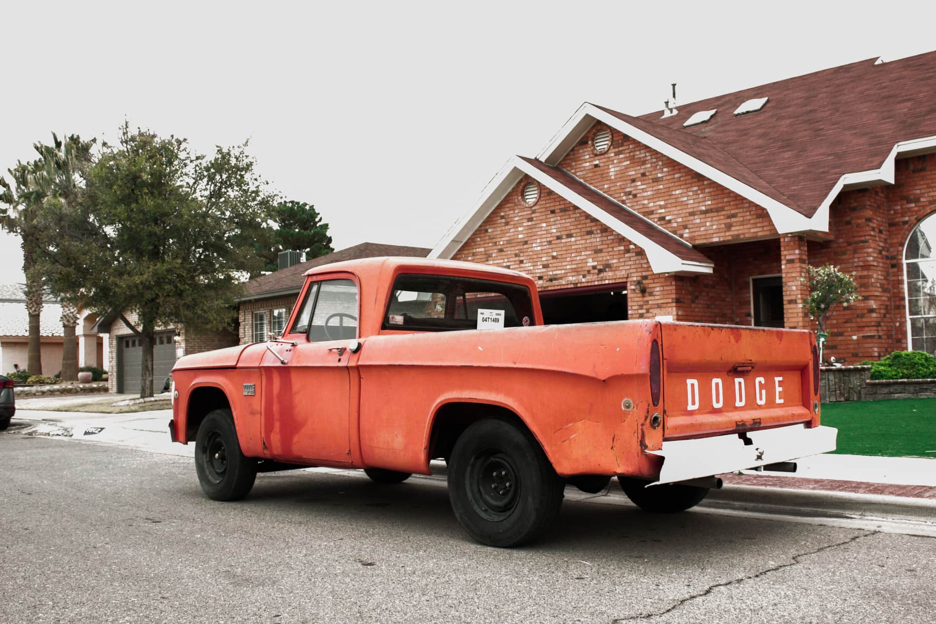 An orange pickup truck parked outside a brick house