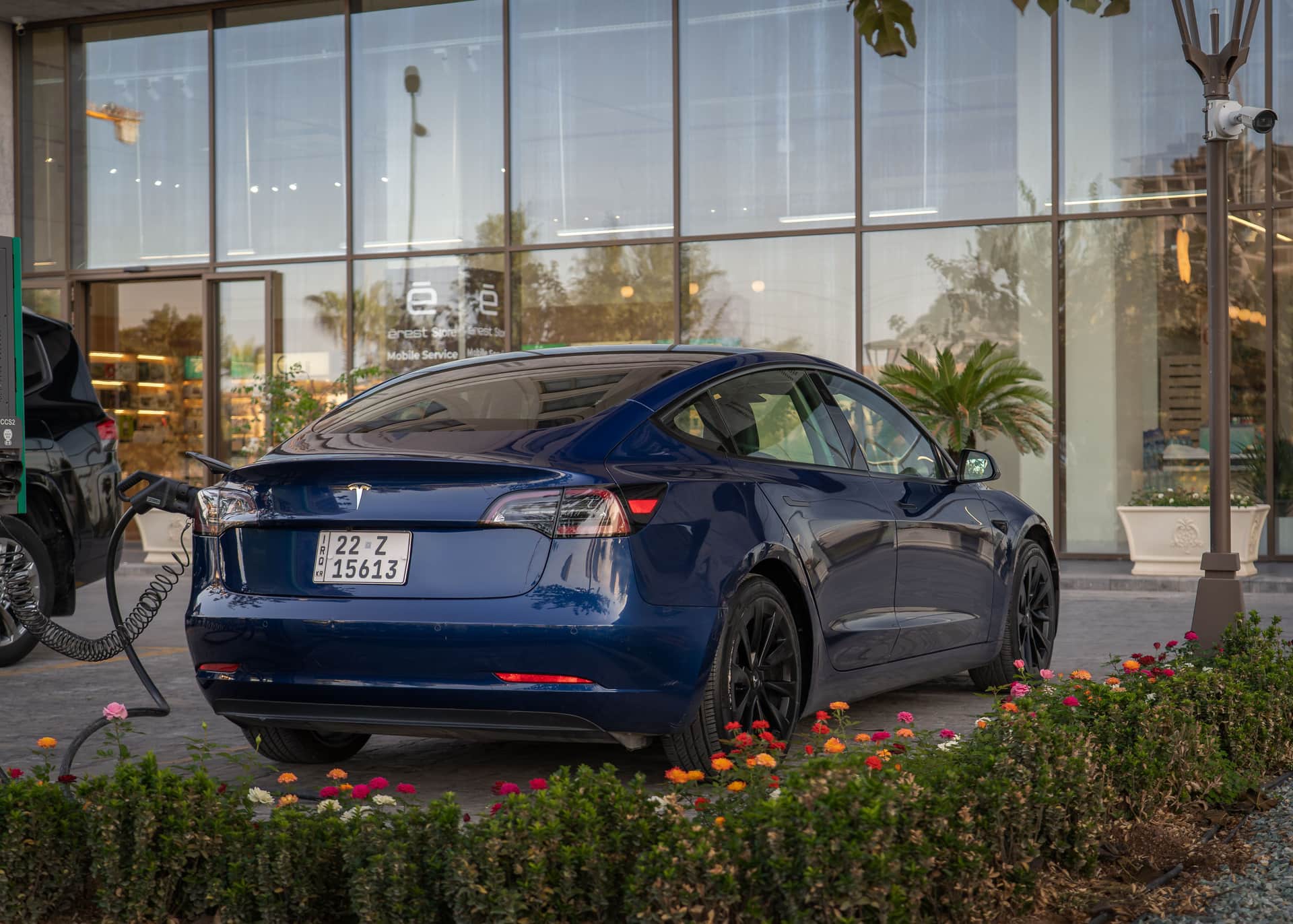 A blue Tesla sedan plugged in to charge outside a building