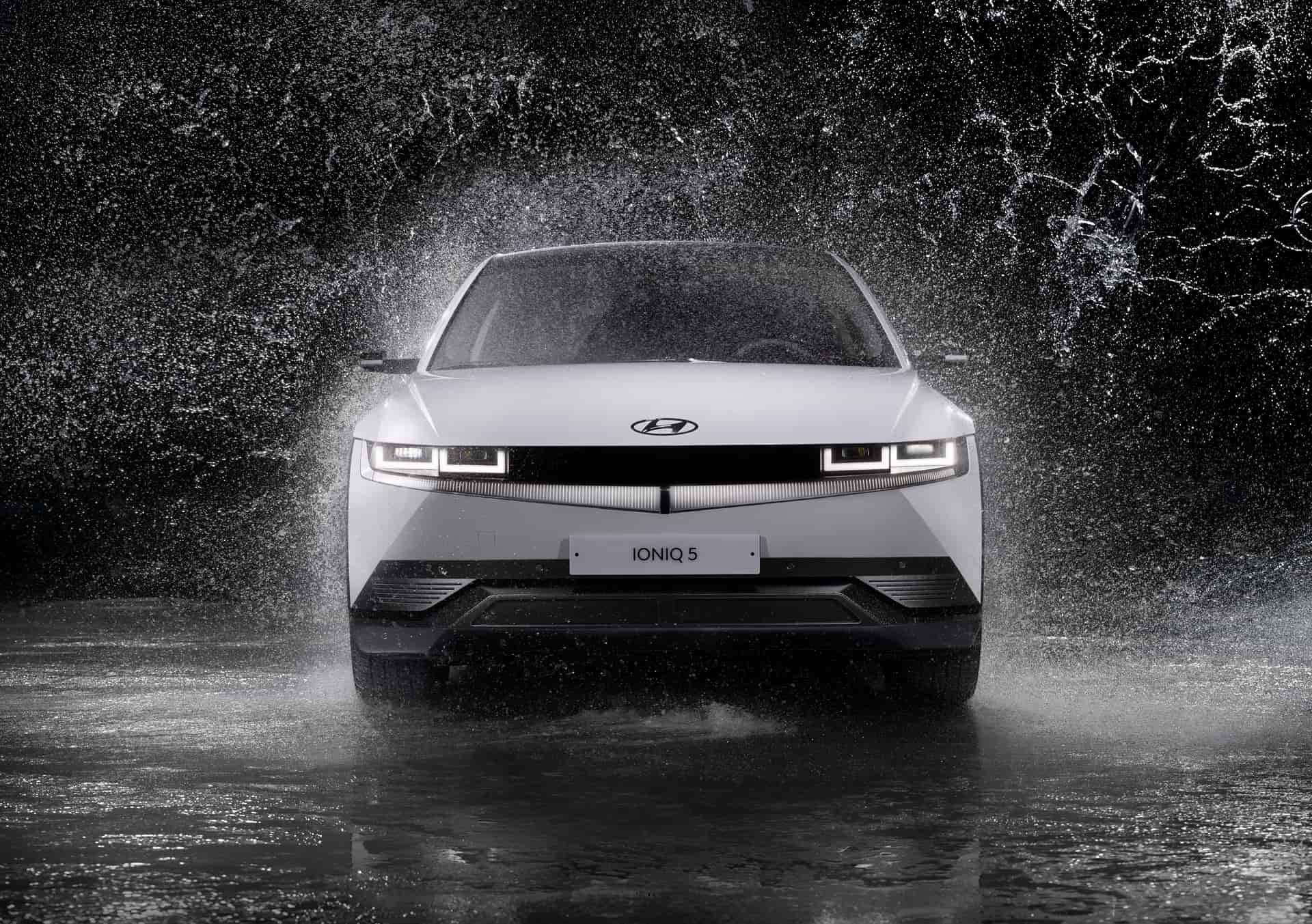 A white Hyundai Ioniq 5 driving through spray on a dark set