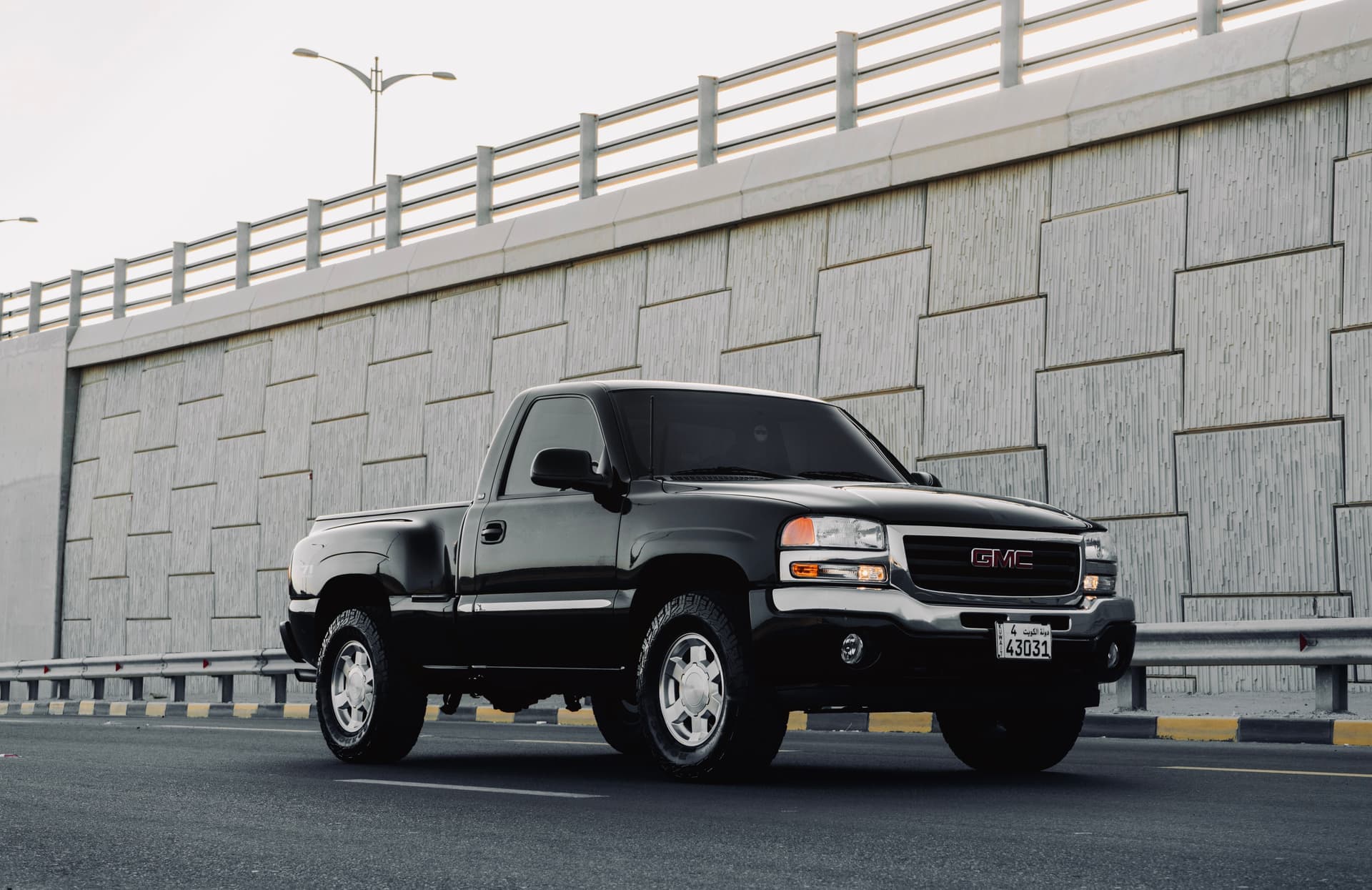A black GMC Sierra pickup truck parked on a road beside a concrete wall