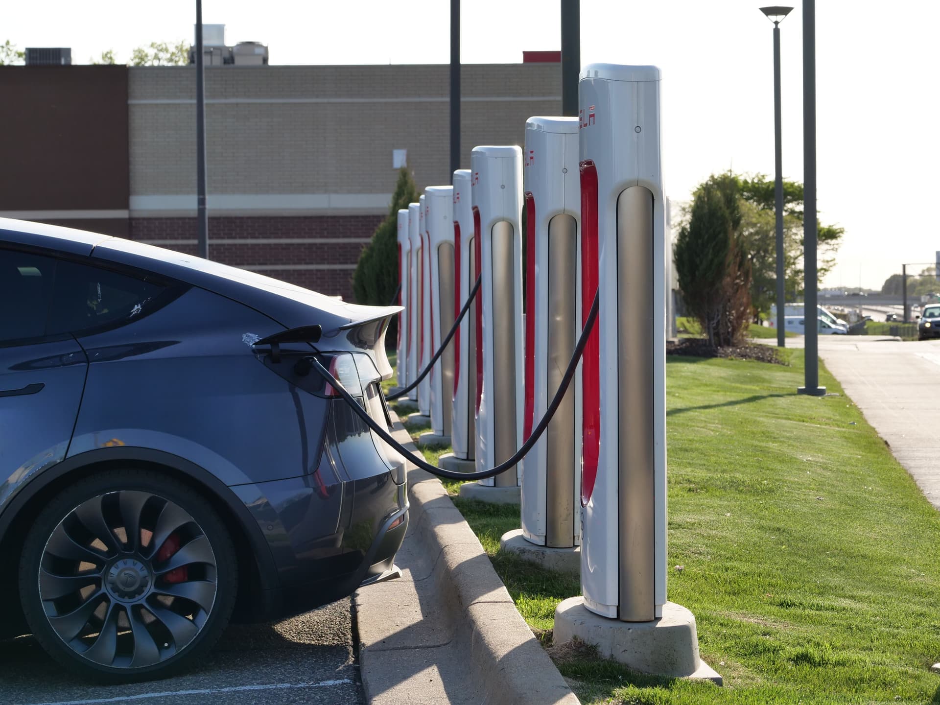A gray Tesla Model Y plugged in at a row of Supercharger posts