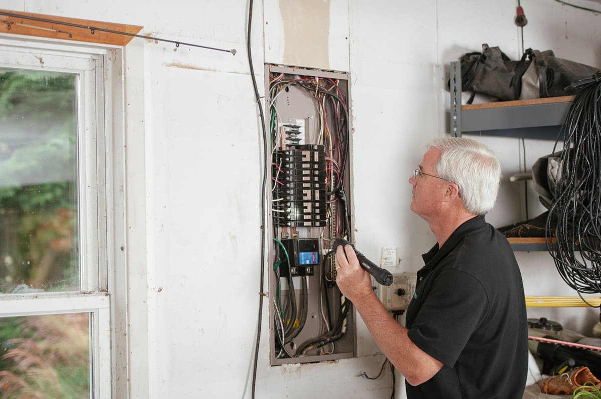 An electrician working at an open residential electrical breaker panel